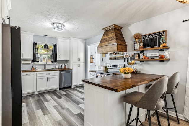 kitchen featuring appliances with stainless steel finishes, sink, butcher block counters, hardwood / wood-style floors, and white cabinets