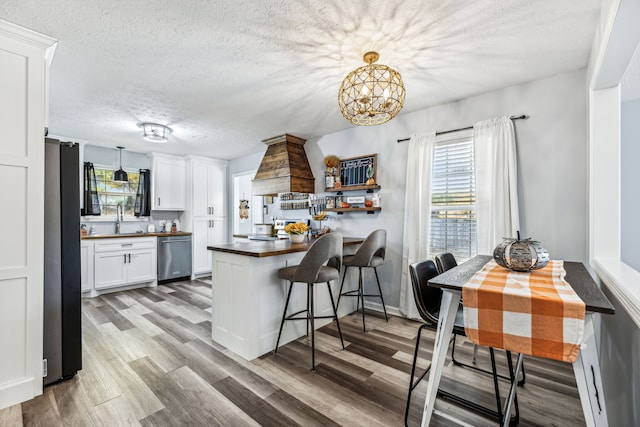 kitchen with white cabinets, hanging light fixtures, stainless steel appliances, and hardwood / wood-style flooring