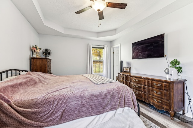 bedroom with light hardwood / wood-style flooring, a textured ceiling, a raised ceiling, and ceiling fan