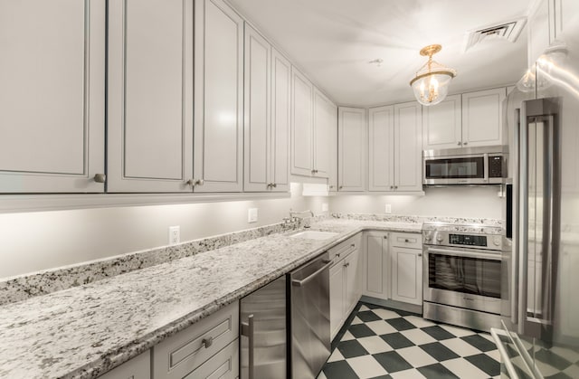 kitchen featuring appliances with stainless steel finishes, sink, white cabinetry, decorative light fixtures, and light stone counters