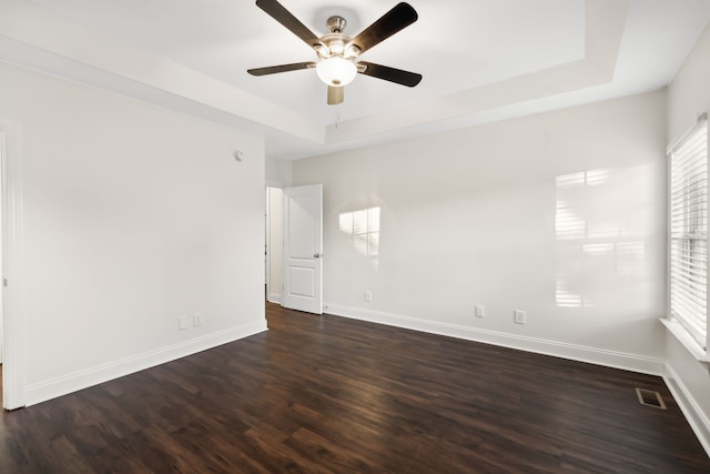 spare room with a raised ceiling, ceiling fan, and dark wood-type flooring