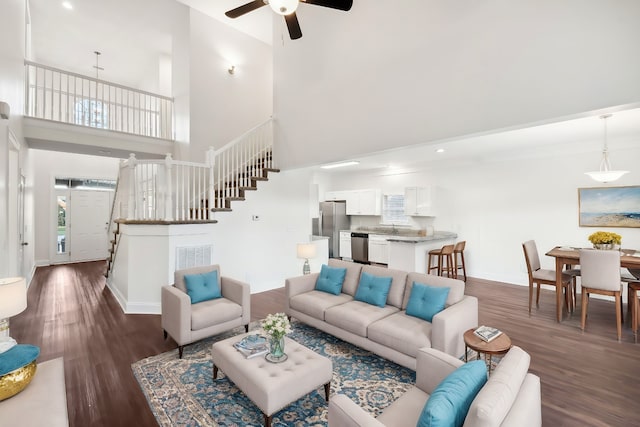 living room with ceiling fan, a towering ceiling, and dark wood-type flooring