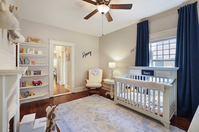 bedroom featuring dark wood-type flooring, a nursery area, and ceiling fan