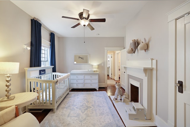 bedroom with a nursery area, wood-type flooring, and ceiling fan