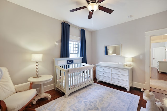 bedroom featuring dark hardwood / wood-style floors, a crib, and ceiling fan