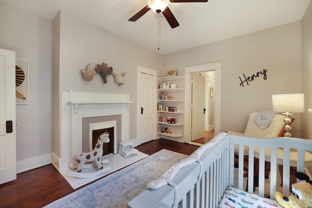 bedroom featuring a crib, dark wood-type flooring, and ceiling fan