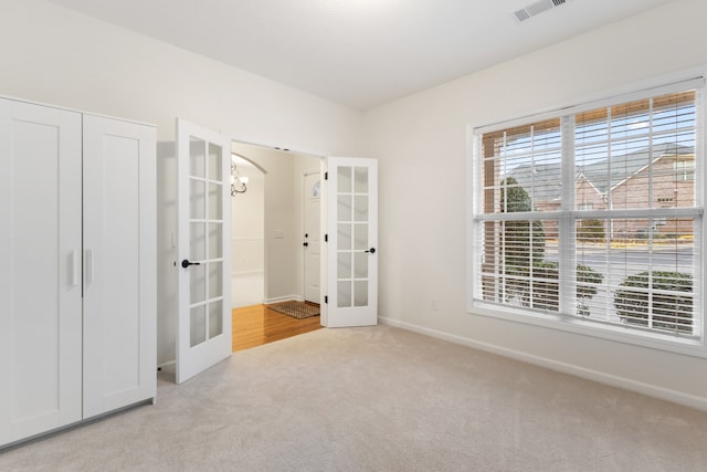 unfurnished bedroom with a closet, light carpet, french doors, and a chandelier