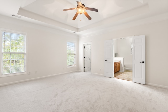 unfurnished bedroom with a raised ceiling, ensuite bath, ceiling fan, and light carpet