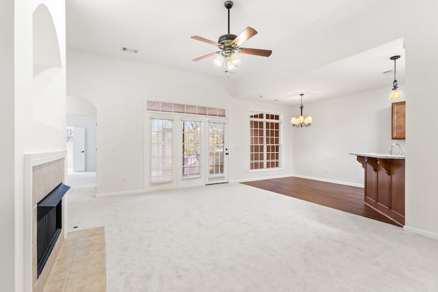 unfurnished living room with ceiling fan with notable chandelier, light colored carpet, sink, and a tiled fireplace