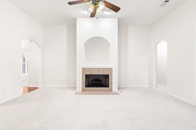 unfurnished living room with light colored carpet, ceiling fan, and a tiled fireplace