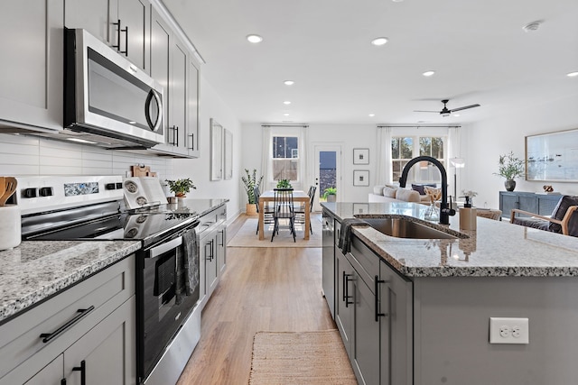 kitchen with light hardwood / wood-style floors, stainless steel appliances, a kitchen island with sink, sink, and gray cabinets