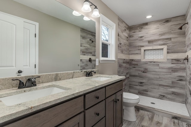 bathroom with toilet, wood-type flooring, vanity, and a tile shower