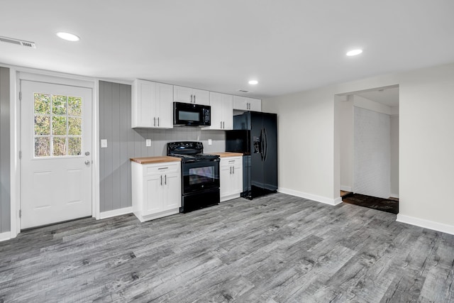 kitchen with butcher block countertops, white cabinetry, black appliances, and light hardwood / wood-style flooring