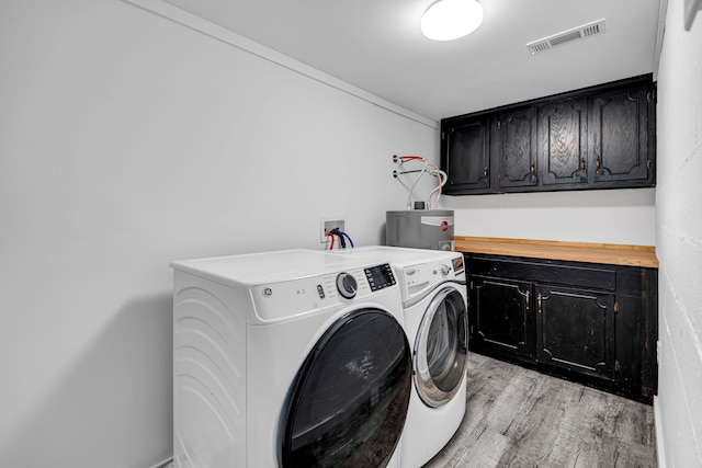 clothes washing area with washer and clothes dryer, cabinets, water heater, and light hardwood / wood-style flooring