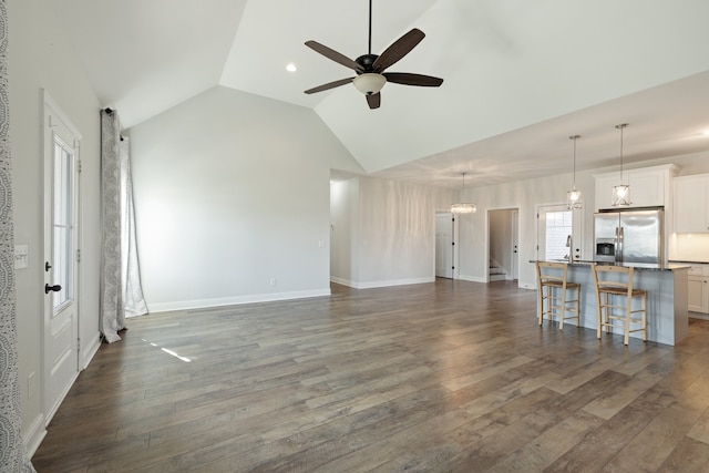 unfurnished living room with vaulted ceiling, dark hardwood / wood-style floors, and ceiling fan with notable chandelier