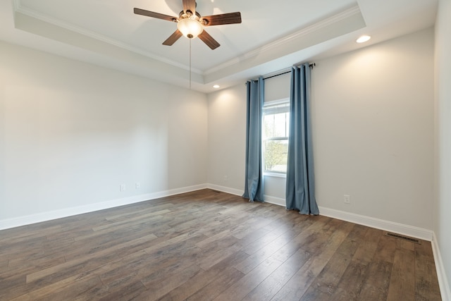 empty room with ornamental molding, dark wood-type flooring, a tray ceiling, and ceiling fan