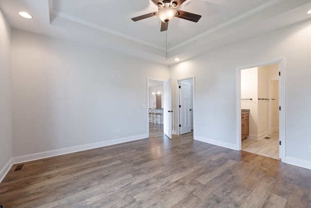 unfurnished bedroom with hardwood / wood-style flooring, a tray ceiling, crown molding, ensuite bathroom, and ceiling fan