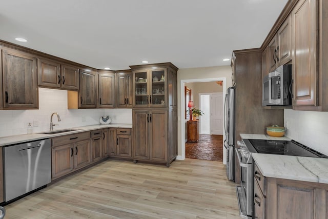 kitchen with appliances with stainless steel finishes, sink, backsplash, and light hardwood / wood-style floors