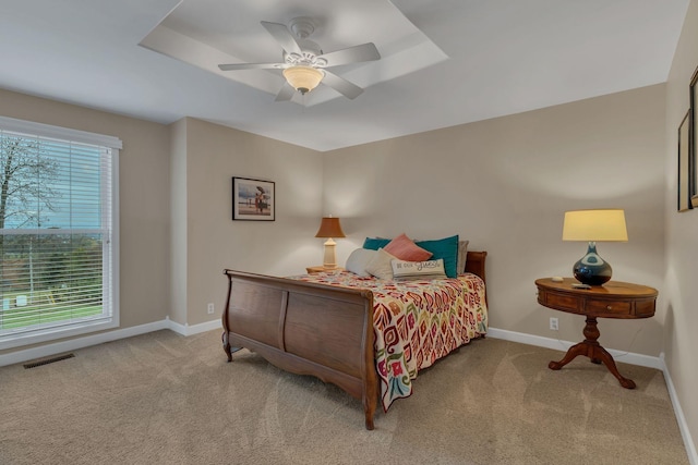 carpeted bedroom with ceiling fan and a tray ceiling