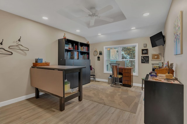 home office with a raised ceiling, ceiling fan, and light hardwood / wood-style flooring