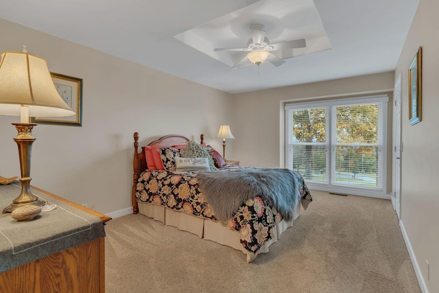 bedroom with light colored carpet, a raised ceiling, and ceiling fan