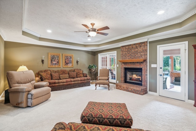 living room featuring a brick fireplace, carpet flooring, crown molding, and a tray ceiling