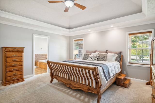 carpeted bedroom with ensuite bath, ceiling fan, crown molding, and a tray ceiling