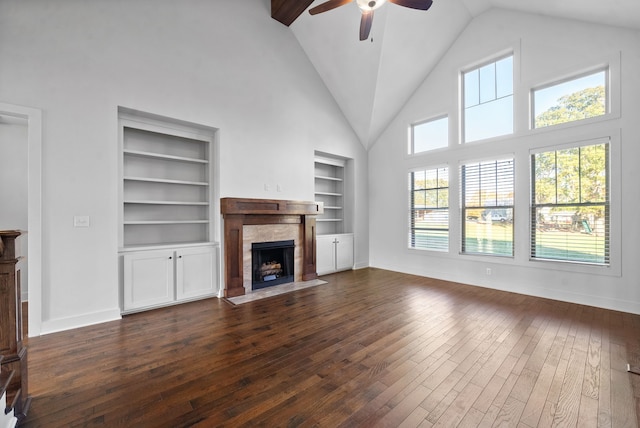 unfurnished living room with a fireplace, dark hardwood / wood-style floors, built in shelves, high vaulted ceiling, and ceiling fan