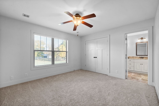 unfurnished bedroom with ceiling fan, connected bathroom, sink, a closet, and light colored carpet