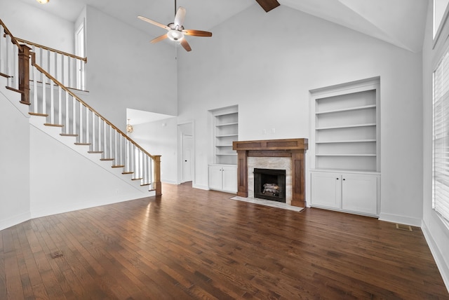 unfurnished living room with built in shelves, high vaulted ceiling, a tile fireplace, and dark hardwood / wood-style flooring