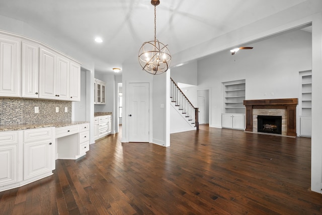 kitchen with a tile fireplace, hanging light fixtures, white cabinets, light stone counters, and dark hardwood / wood-style floors