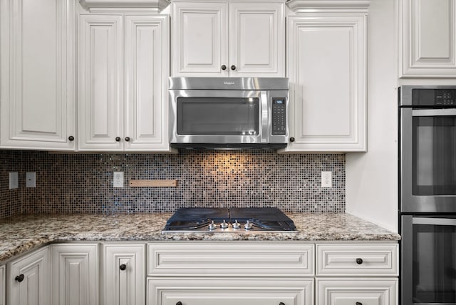 kitchen featuring appliances with stainless steel finishes, light stone counters, white cabinets, and tasteful backsplash