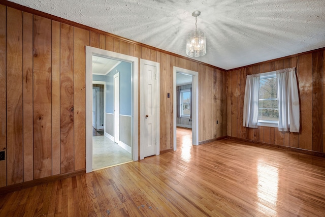 unfurnished room featuring a textured ceiling, light wood-type flooring, an inviting chandelier, and wooden walls