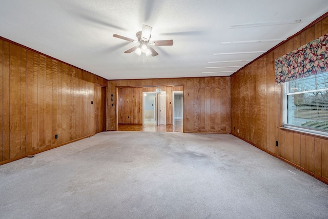 empty room featuring ceiling fan, wood walls, and light colored carpet