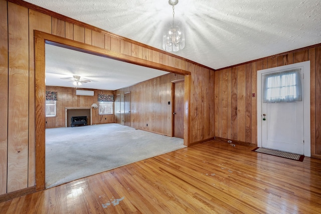 unfurnished living room with ceiling fan with notable chandelier, a textured ceiling, light hardwood / wood-style floors, and wood walls