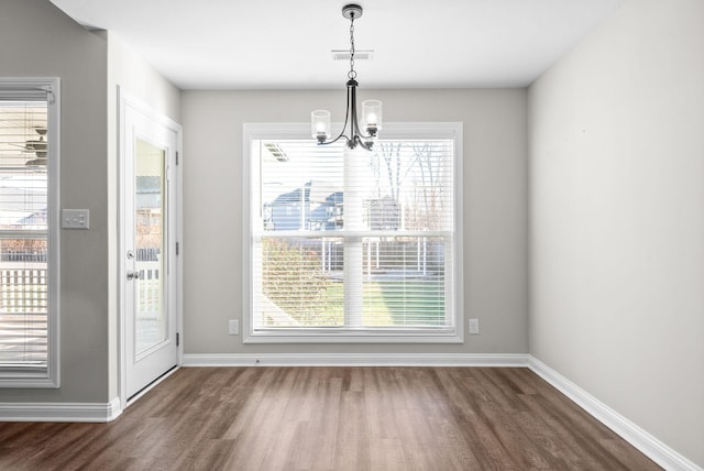 unfurnished dining area featuring a chandelier, dark hardwood / wood-style floors, and a wealth of natural light