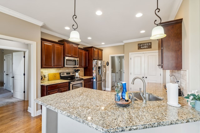 kitchen with stainless steel appliances, sink, decorative light fixtures, light stone counters, and light hardwood / wood-style floors