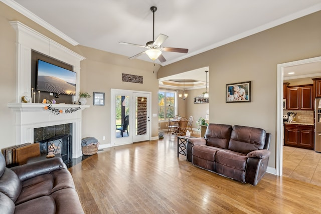 living room with a fireplace, ceiling fan with notable chandelier, light wood-type flooring, and crown molding