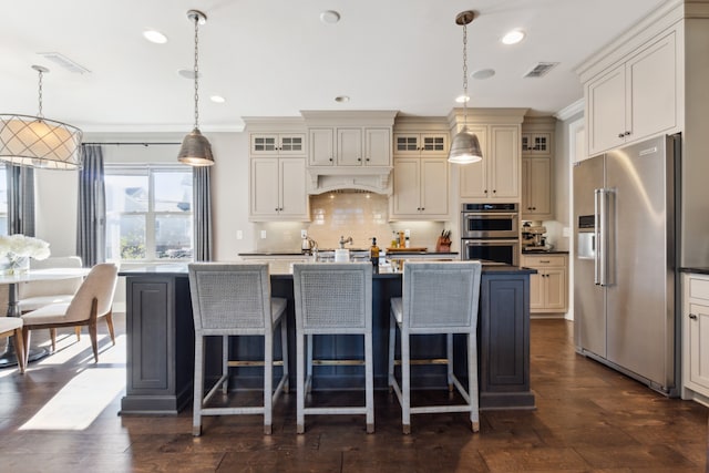 kitchen with appliances with stainless steel finishes, decorative light fixtures, and a kitchen island with sink