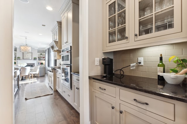 kitchen featuring stainless steel double oven, dark stone countertops, crown molding, dark hardwood / wood-style flooring, and tasteful backsplash