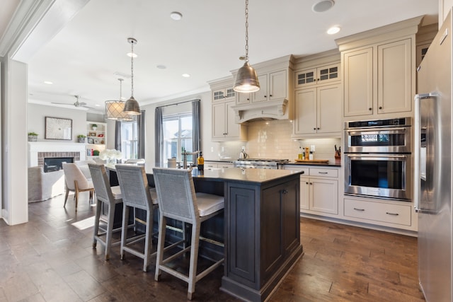 kitchen with cream cabinets, appliances with stainless steel finishes, pendant lighting, and a brick fireplace