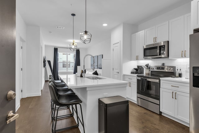 kitchen featuring appliances with stainless steel finishes, decorative light fixtures, white cabinetry, and an island with sink