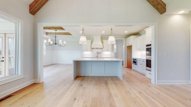 kitchen with pendant lighting, an island with sink, white cabinets, custom exhaust hood, and stainless steel double oven