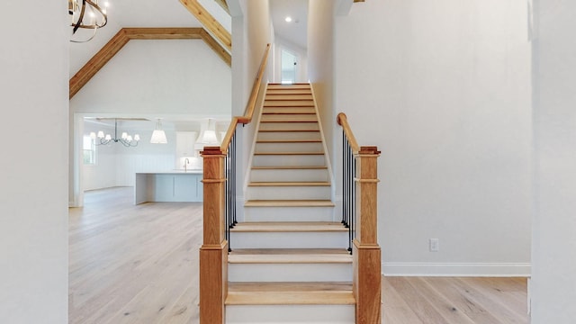 stairway featuring hardwood / wood-style flooring, a towering ceiling, sink, and a notable chandelier