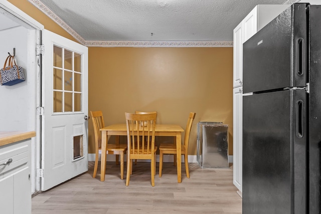 dining space featuring ornamental molding, light hardwood / wood-style flooring, and a textured ceiling