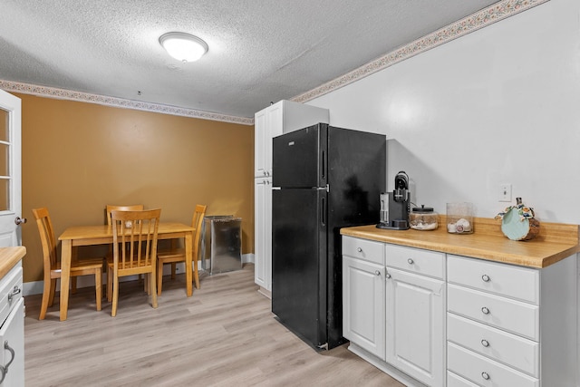 kitchen featuring white cabinetry, a textured ceiling, light hardwood / wood-style flooring, and black fridge