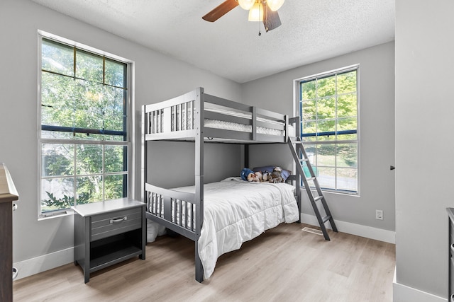 bedroom featuring light hardwood / wood-style flooring, a textured ceiling, multiple windows, and ceiling fan