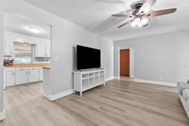 unfurnished living room with ceiling fan, a textured ceiling, and light wood-type flooring