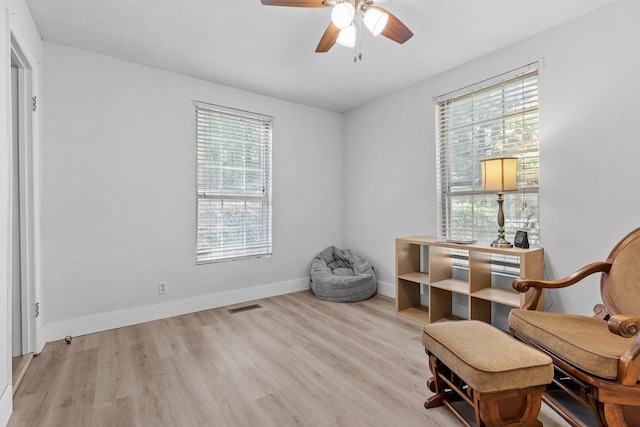 living area featuring a textured ceiling, ceiling fan, light wood-type flooring, and a wealth of natural light