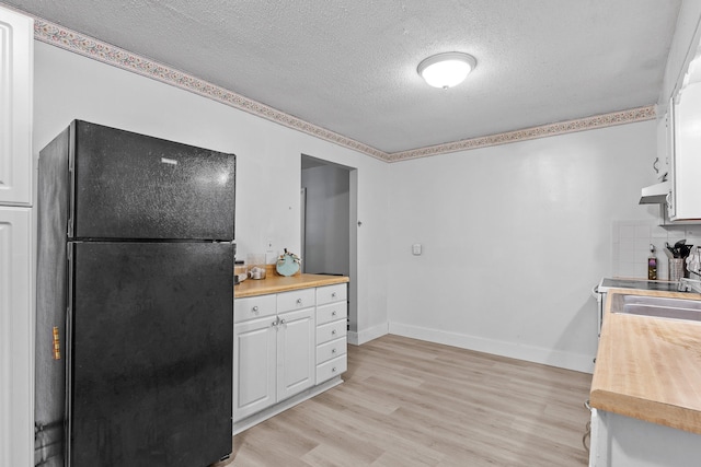 kitchen featuring wooden counters, black refrigerator, white cabinetry, and light hardwood / wood-style floors